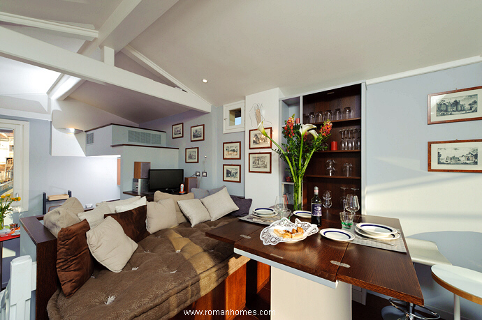 Closer view of the dining table, of the nearby shelves, and of the sofa bed where from you an either have lunch or relax watching the views